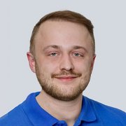 Ein junger Mann mit einem freundlichen Lächeln trägt ein blaues Hemd und hat einen gepflegten Bart.