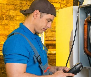 Ein Techniker in blauer Arbeitskleidung überprüft eine Maschine mit einem Handgerät in einer gut beleuchteten Umgebung.