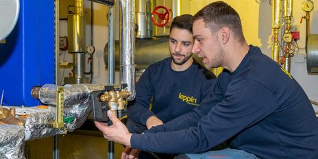 Zwei Techniker arbeiten konzentriert an einer Heizungsanlage, während sie ein Ventil in der Hand halten und diskutieren.