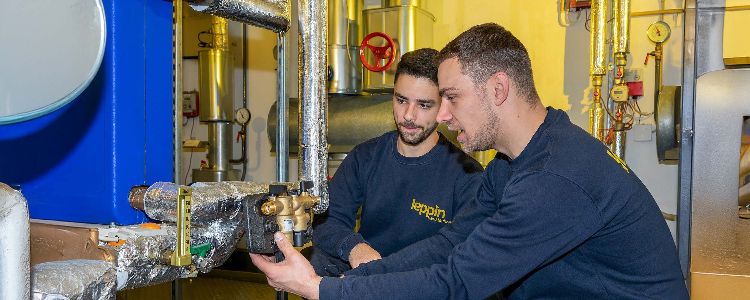 In einem technischen Raum überprüfen zwei Männer gemeinsam ein Ventil, um sicherzustellen, dass alles korrekt funktioniert.