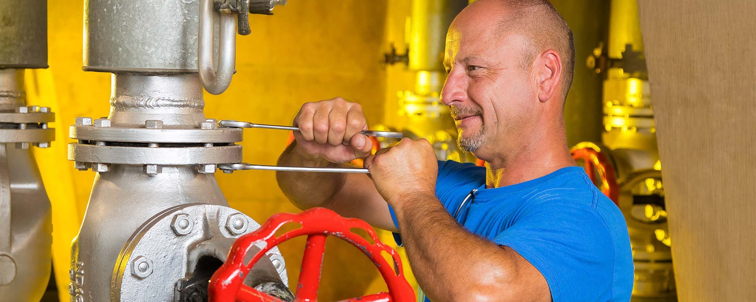 Ein Handwerker arbeitet konzentriert an einem großen Ventil, während er mit einem Schraubenschlüssel die Schrauben festzieht.