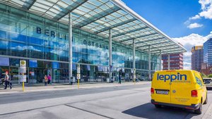 Passanten schlendern vor dem Berliner Ostbahnhof, dessen große Fensterfront das Tageslicht eindrucksvoll einfängt.
