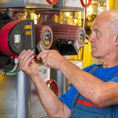 Der Mann in blauer Kleidung arbeitet an einer Maschine, während er präzise mit Werkzeugen hantiert.