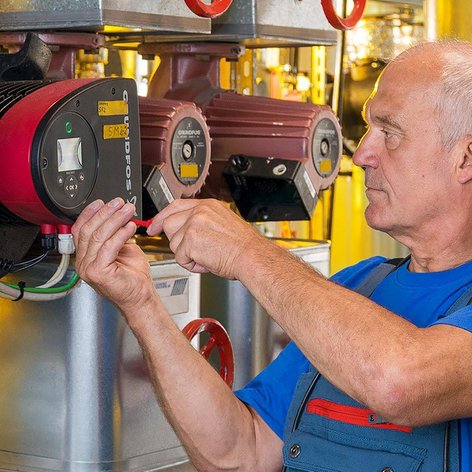 Der Mann in blauer Kleidung arbeitet an einer Maschine, während er präzise mit Werkzeugen hantiert.