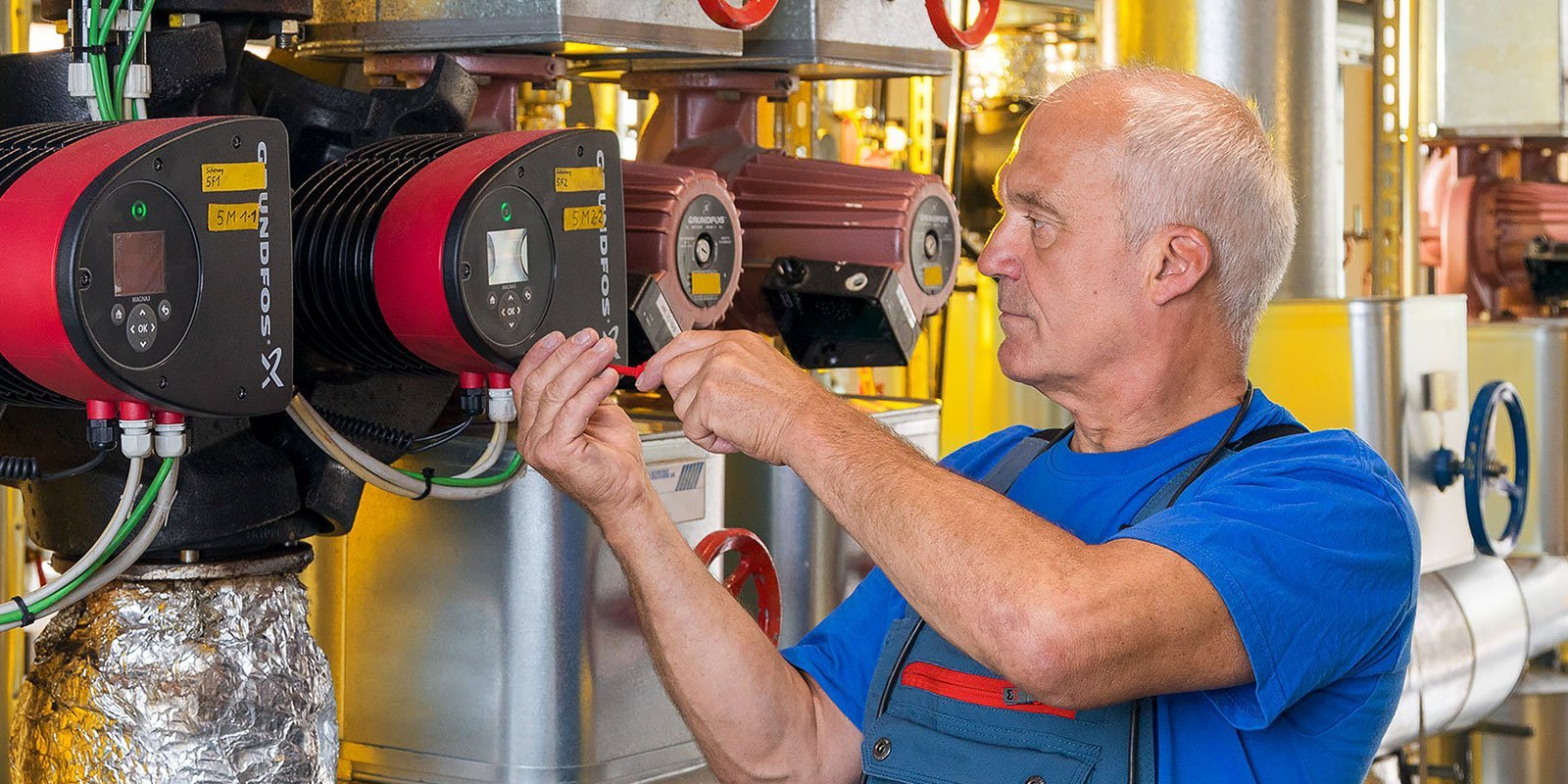 Der Mann in blauer Kleidung arbeitet an einer Maschine, während er präzise mit Werkzeugen hantiert.