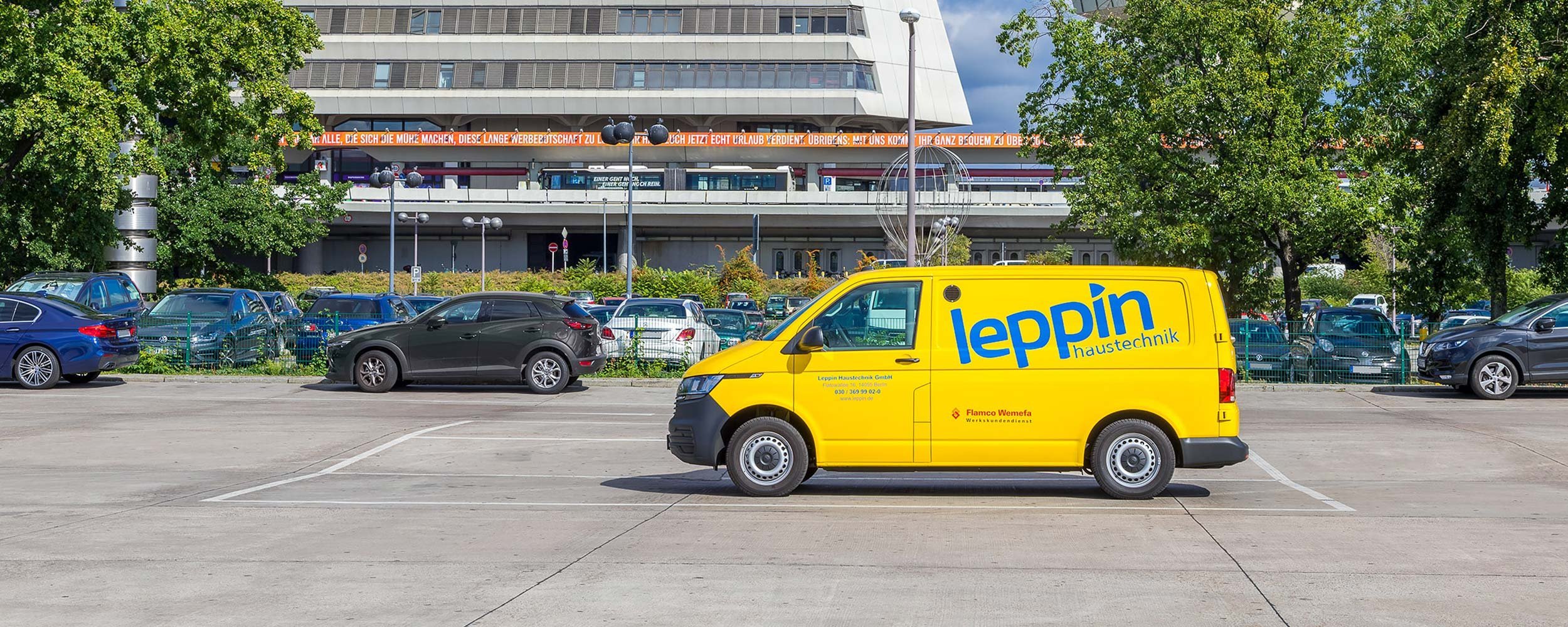 Ein gelber Lieferwagen mit der Aufschrift 'leppin haustechnik' parkt auf einem weitläufigen Parkplatz, umgeben von Bäumen.