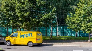 Ein gelbes Fahrzeug mit dem Logo 'leppin' steht an einer Straße, während im Hintergrund ein modernes, lichtdurchflutetes Gebäude sichtbar ist.