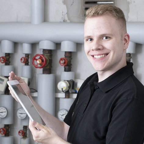 Ein Anlagenmechaniker vor einer Heizungsanlage mit einem Tablet