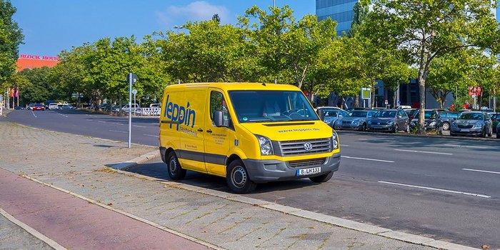 Ein gelber Lieferwagen mit der Aufschrift 'Heizungstechnik' parkt an einer belebten Straße, umgeben von Bäumen und anderen Fahrzeugen.