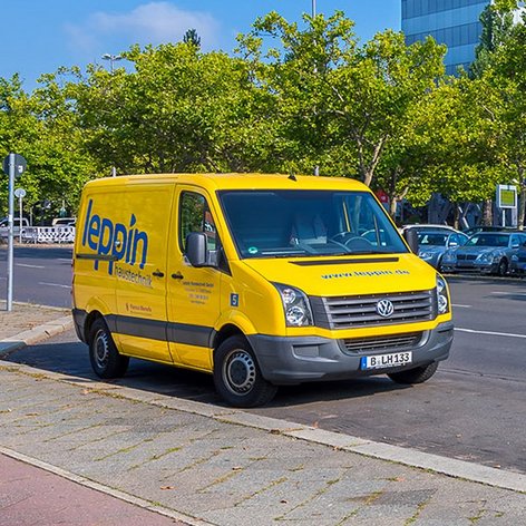 Ein gelber Lieferwagen mit der Aufschrift 'Heizungstechnik' parkt an einer belebten Straße, umgeben von Bäumen und anderen Fahrzeugen.
