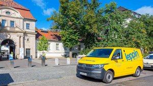 Ein gelber Lieferwagen steht vor einem historischen Gebäude mit einer beeindruckenden Fassade und blauen Himmel im Hintergrund.