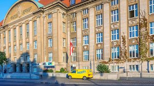 Ein gelbes Lieferfahrzeug parkt vor einem beeindruckenden historischen Gebäude mit vielen Fenstern und kunstvollen Details.