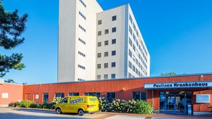 Vor dem Paulinen Krankenhaus parkt ein gelbes Fahrzeug, während die Sonne auf die moderne Architektur und die Umgebung scheint.